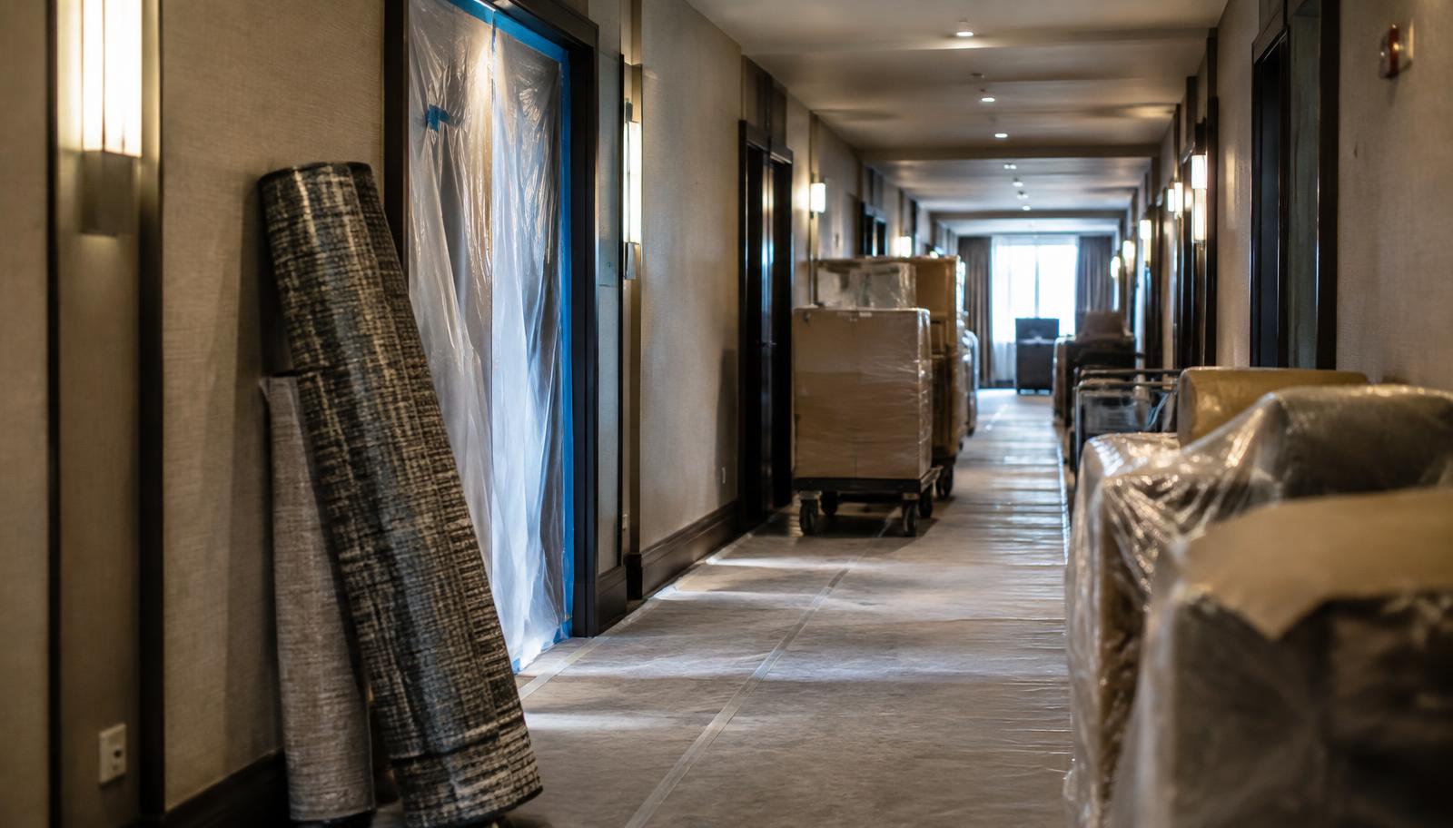 Hotel guest corridor under renovation with carpet rolls, dust barrier and wrapped furniture carts
